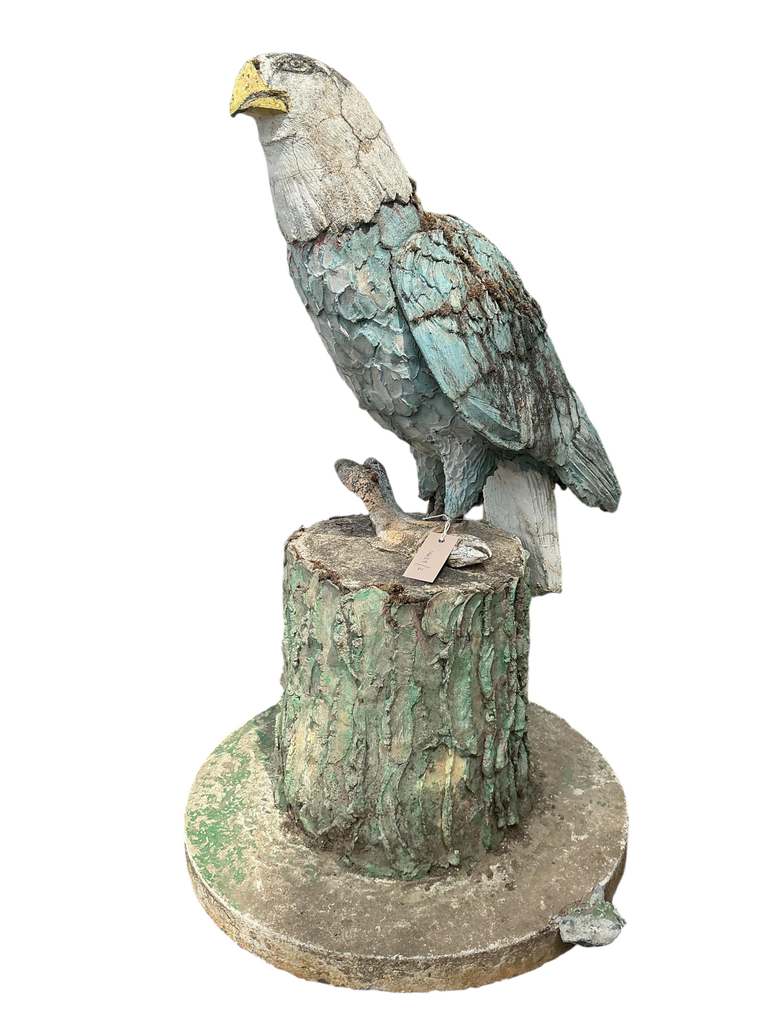 A cast stone garden ornament of an eagle perched on a stump with a salmon in its talons, on square wood plinth, height 150cm